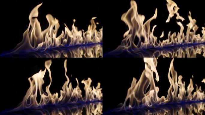 在黑色反射背景上，火以慢动作点燃并燃烧。易燃燃料或汽油的污渍在黑暗中燃烧释放能量和蓝光。火光