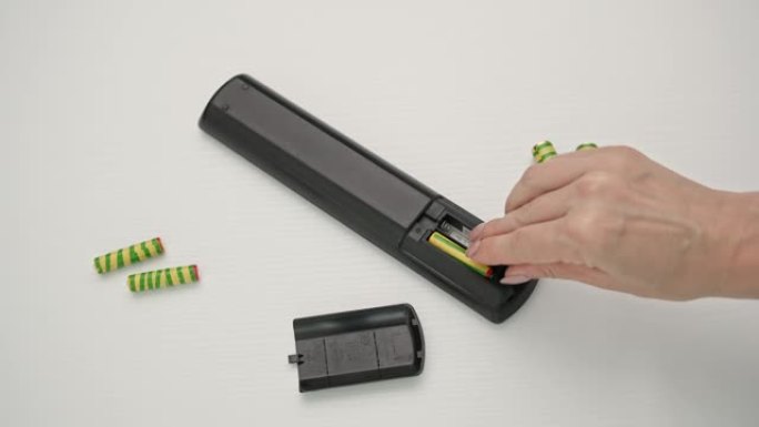 年轻女子将电池放在木制背景上的遥控器中，俯视图