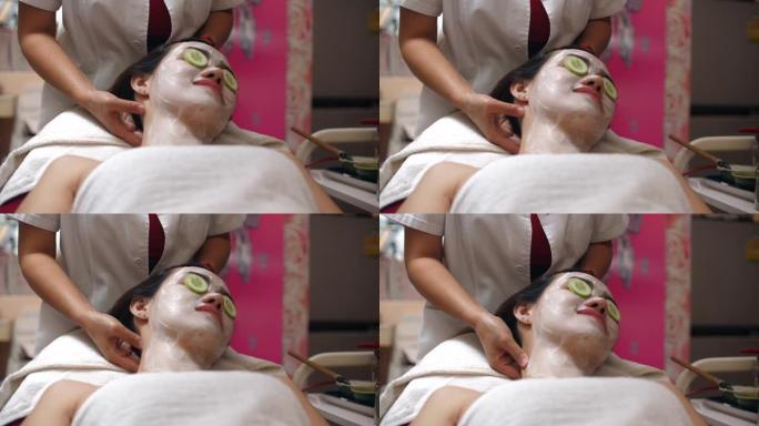 美丽的年轻女子在水疗中心戴着口罩，眼睛里躺着黄瓜