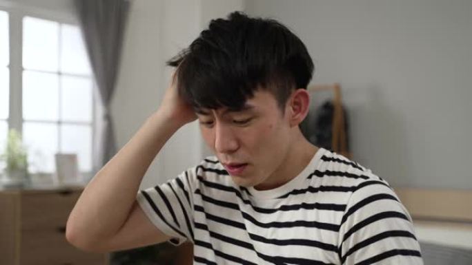 愤怒的亚洲男性在家里的卧室里做一件重要的工作时，一边抓着头发一边咒骂，感觉被他崩溃的电脑惹恼了。