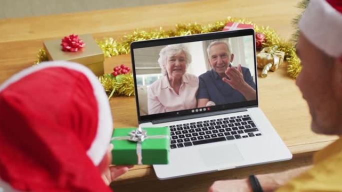 戴着圣诞老人帽子的高加索父子使用笔记本电脑与家人在屏幕上进行圣诞节视频通话