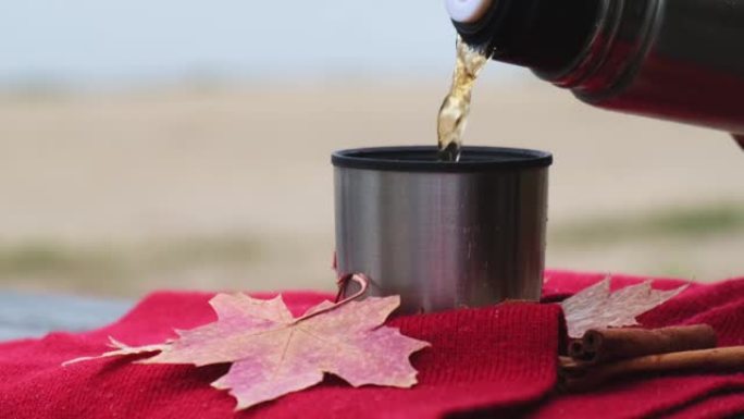 秋季公园室外热杯倒入热茶。红领巾秋季野餐保温瓶