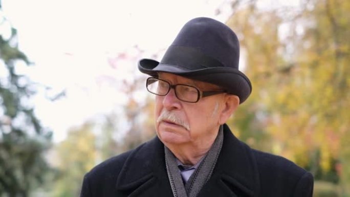 公园里孤独的爷爷，穿着黑色外套和黑色帽子。