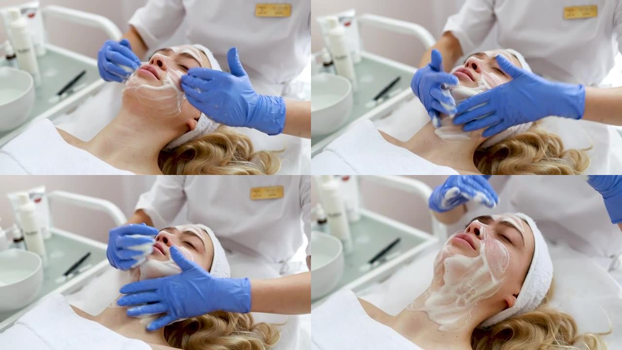美容师医生正在在女人的脸上涂抹洁面泡沫。美容诊所的面部皮肤按摩