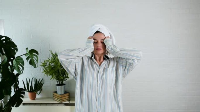 穿着睡衣的年轻美女，湿漉漉的头发包裹在毛巾上，用手在室内看着镜头，表现出头脑风暴或令人振奋的手势或反
