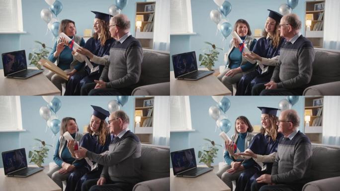 在线毕业典礼，穿着学术礼服和帽子的快乐女毕业生与父母在远程学习期间坐在家里被授予文凭