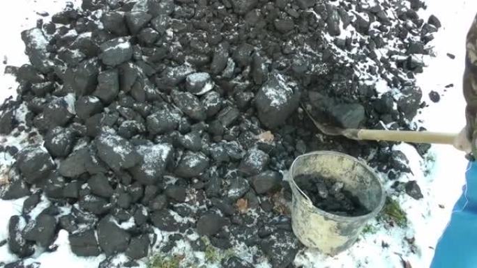 冬天，一个人用铁锹将煤块铲入桶中。锅炉的燃料。