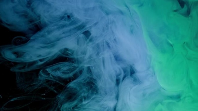蓝色和绿色的油漆滴落在黑色背景的水中，抽象的颜色混合，水墨漆滴落在水上。