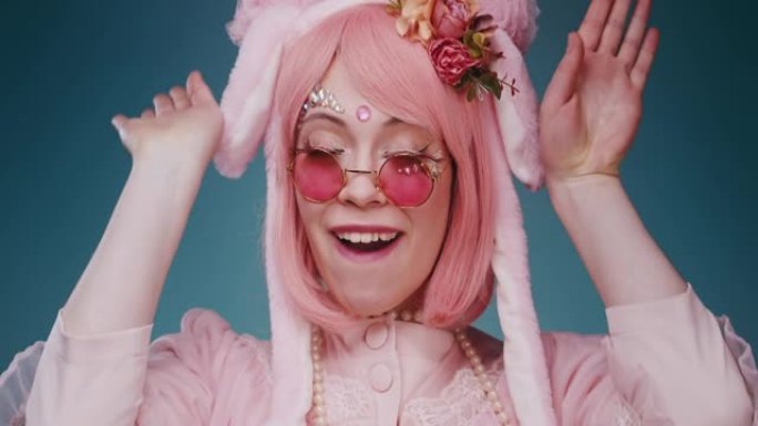 粉红色可爱的糖果动漫女孩与兔子耳朵和粉红色太阳镜的特写镜头使情感的鬼脸和挥舞她的耳朵孤立在蓝色背景。