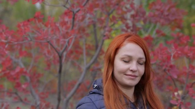 秋天，一个红色头发的生活方式女人的肖像，手里拿着智能手机，背景是五颜六色的树叶