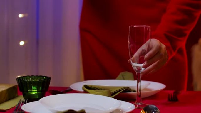 穿着红色连衣裙的女人在盘子和餐具旁边的节日桌子上放置了两杯香槟。家庭舒适的房间，为庆祝新年或圣诞节而