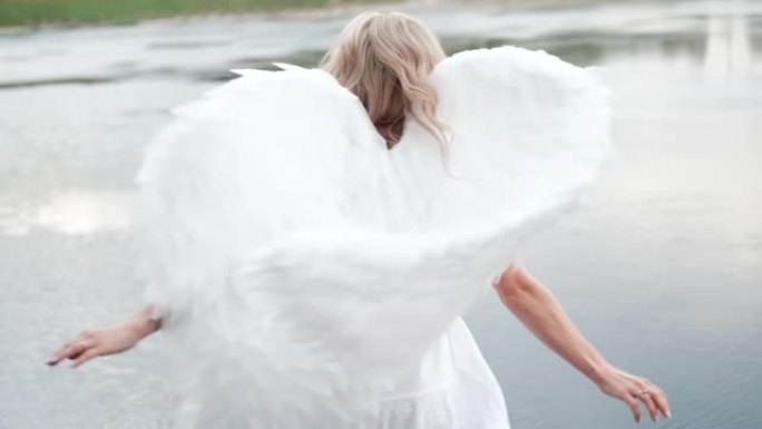 穿着白色连衣裙的美丽天使。惊人的金发女人，长长的卷发和白色的翅膀。慢动作