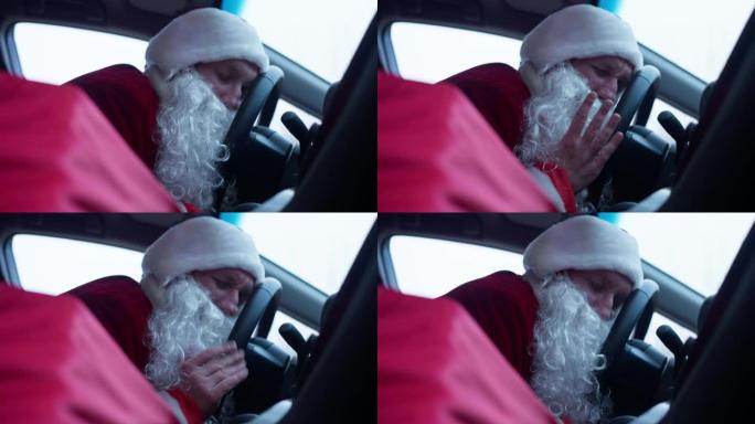 疲惫的圣诞老人睡在车里，头靠在方向盘上。新年前夕，穿着红色服装的年轻疲惫的白人男子在汽车上小睡的肖像