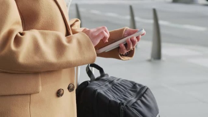 在智能手机中，在机场停车场的户外，穿着时尚的米色羊绒大衣，在没有人脸搜索信息的女人周围的相机的圆形飞