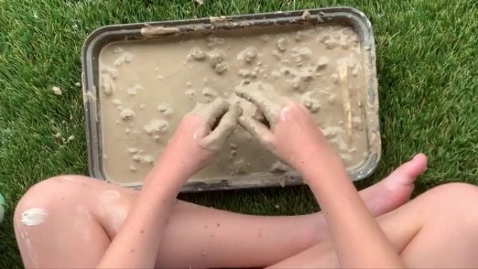 一个孩子的特写镜头，湿的，泥泞的手和肮脏的飞溅的腿和手臂，在玩湿的模型粘土时弄得一团糟。慢动作。