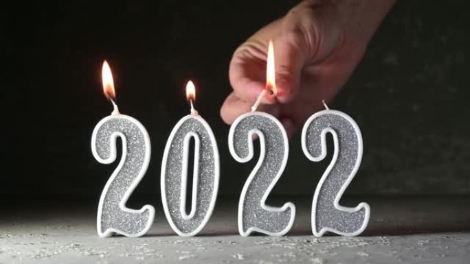一只女性的手在黑暗的背景上2022数字的形式点燃银蜡烛。