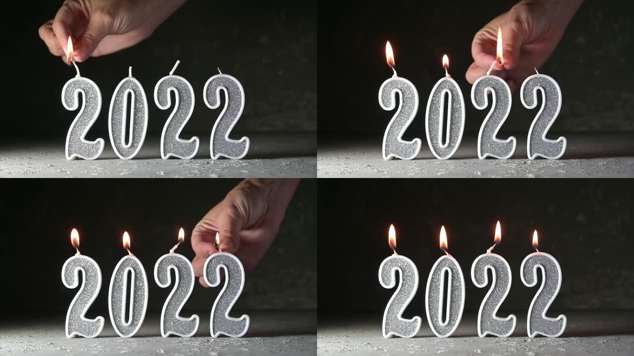 一只女性的手在黑暗的背景上2022数字的形式点燃银蜡烛。