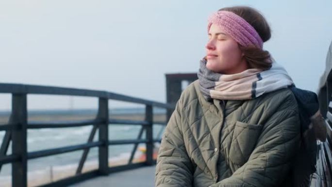 穿着暖和衣服的女人在冬天的海边呼吸新鲜空气。旅行者女人在淡季在海边，4k 60p