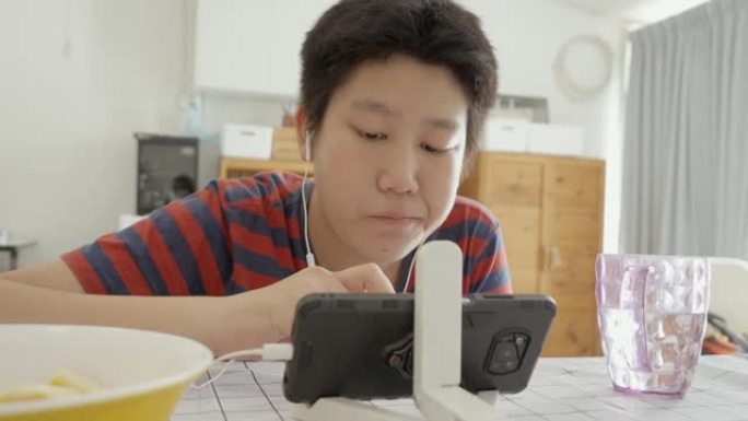 亚洲男孩在家里用智能手机看电影或YouTube视频时吃一块苹果，生活方式概念。