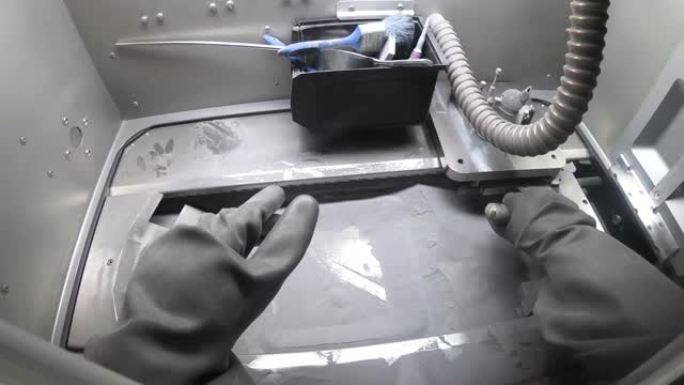 工人在工作室3D金属打印机内戴着孤立的橡胶手套。从金属3D打印机的工作平台上拿出工具并倒入金属粉末。