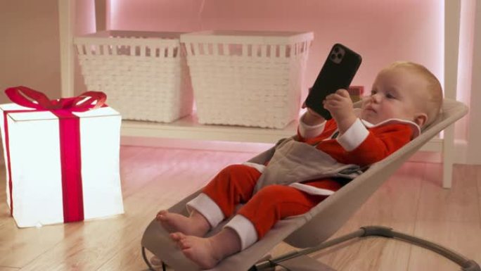穿着圣诞老人的孩子在除夕夜用智能手机玩得开心，快乐的孩子庆祝他的第一个新年。可爱的男婴拿着手机看着触
