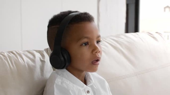 坐在沙发上戴着无线耳机听音乐的黑人小男孩