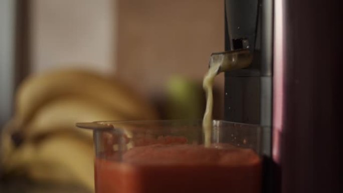 4k离心榨汁机压榨自制胡萝卜汁。用果汁填充塑料杯。制作鲜榨果蔬汁，特写。厨房电器。健康饮料，香蕉，早