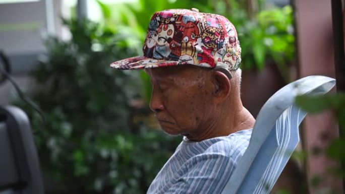 一位九十多岁的亚洲男子坐在家里，一生都在努力工作中放松。