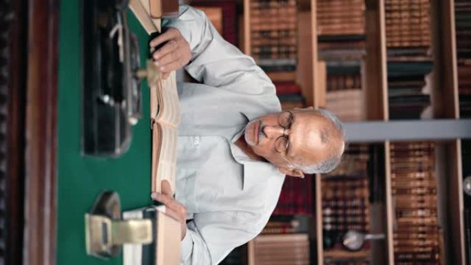 垂直视频POV聚焦的祖父坐在图书馆的桌子上阅读老式纸质教科书