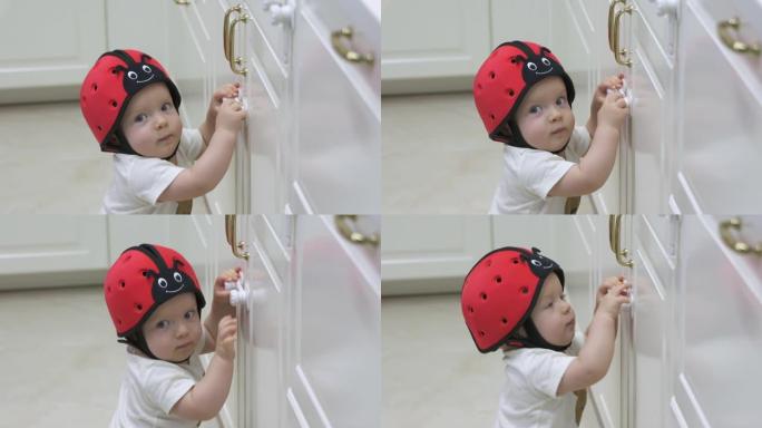 为房屋打气，婴儿戴着安全帽探索厨房橱柜，好奇的小孩试图打开装有儿童安全锁的橱柜门。