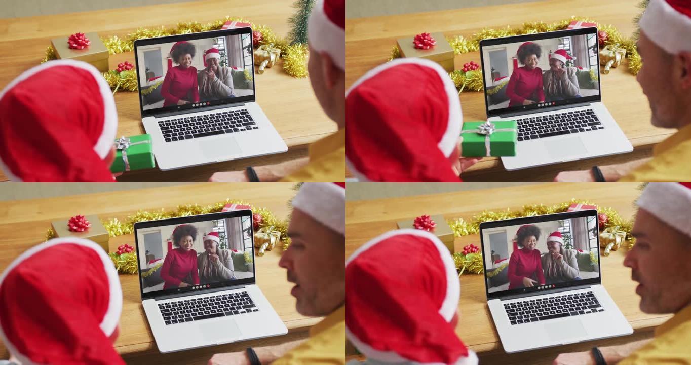 戴着圣诞老人帽子的高加索父子使用笔记本电脑与家人在屏幕上进行圣诞节视频通话