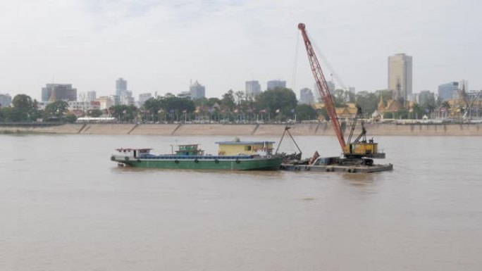 固定在驳船上的抓斗挖泥船停泊在湄公河。金边首都为背景