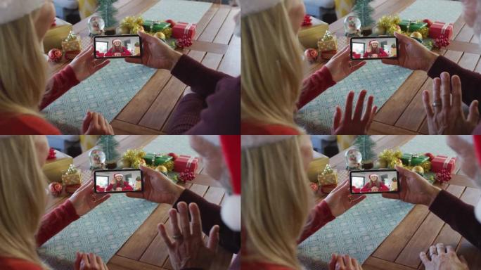 白人夫妇戴着圣诞老人帽子，使用智能手机与屏幕上的女人进行圣诞节视频通话