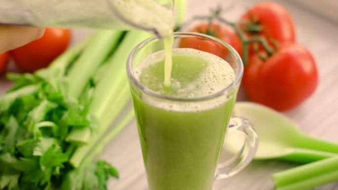 健康的素食绿色芹菜冰沙。背景上有西红柿小枝的芹菜汁。芹菜汁倒入玻璃杯中。慢动作