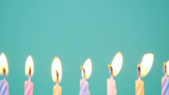 生日快乐概念由在蓝色或绿松石背景上燃烧五颜六色的蜡烛制成。吹灭7周年生日蜡烛。慢动作全高清视频。