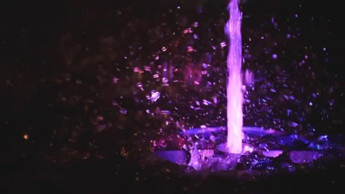 五颜六色的喷泉飞溅。以各种颜色照亮的水的慢动作落在喷泉上，该喷泉在夜间改变了其水色