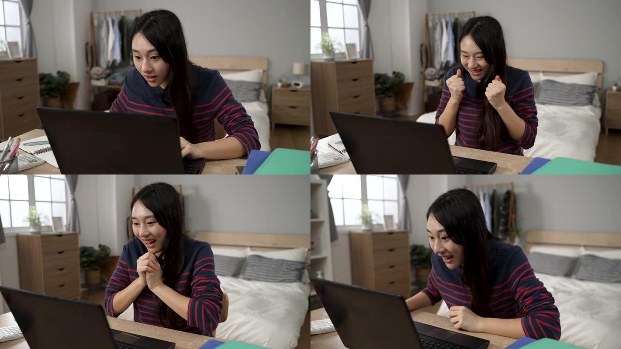 快乐的韩国女学生收到录取通知书电子邮件，握紧拳头，向前倾斜电脑屏幕，在家中查看细节。