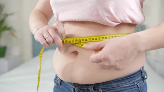 肥胖妇女用黄色卷尺测量大肚子的特写镜头。节食的概念，不健康的生活方式，超重和肥胖