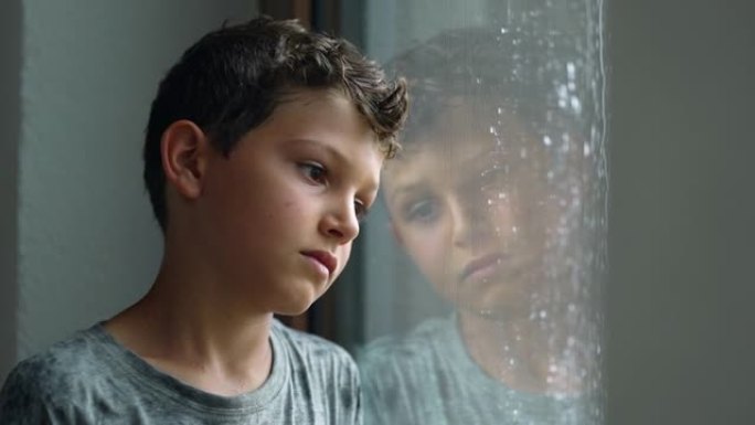 沮丧的小男孩站在窗边。雨天儿童疼痛