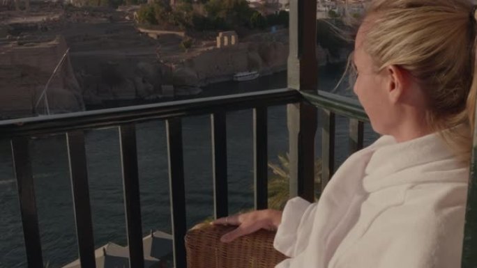 慢动作: 年轻女子在酒店的阳台上穿着浴袍，在埃及阿斯旺 (Aswan) 欣赏壮丽的河景。女性旅行需要