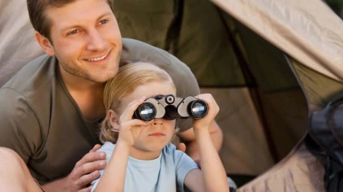 微笑的白人父亲和孩子在帐篷里，孩子用望远镜看鸟