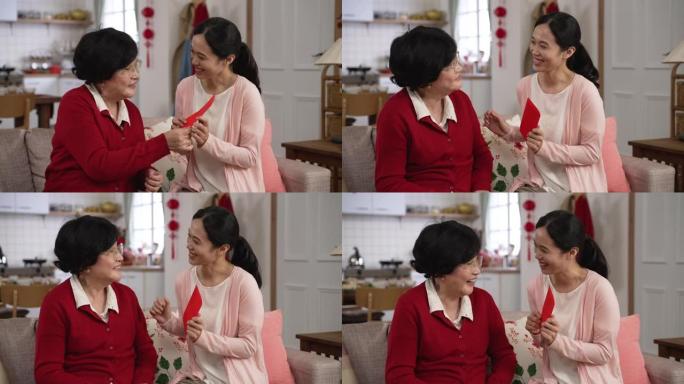 当他们坐在家里的客厅沙发上聊天时，穿着红色衣服的慈爱的亚洲老母亲给儿媳一个红包