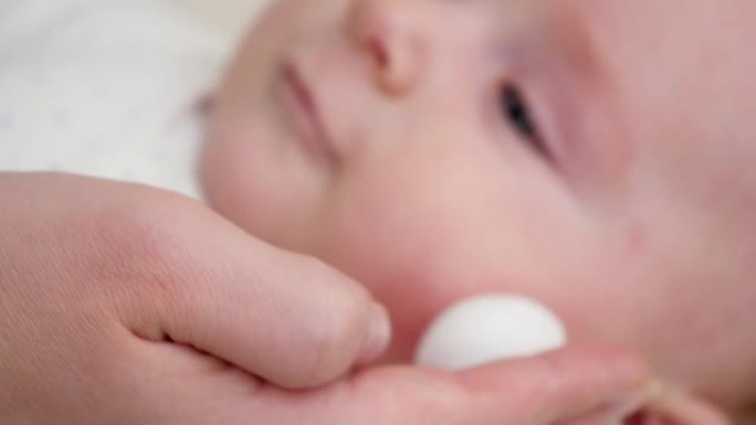 在患有皮炎和痤疮的红色婴儿脸颊上使用药物乳液的特写镜头。新生婴儿卫生、健康和皮肤护理的概念
