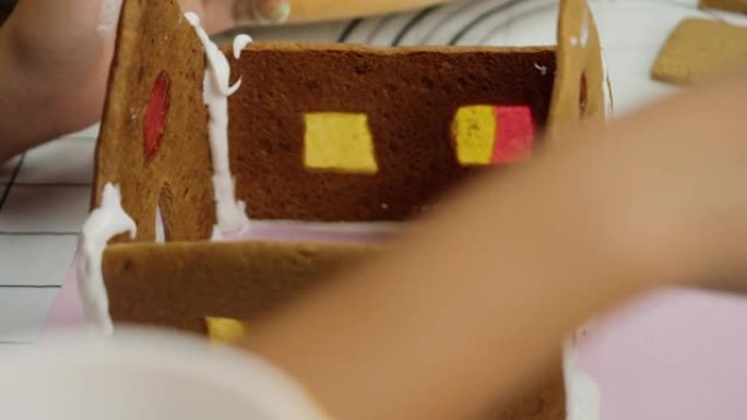 孩子的手在晚上在家与姐姐一起制作姜饼屋，圣诞节庆祝生活方式。