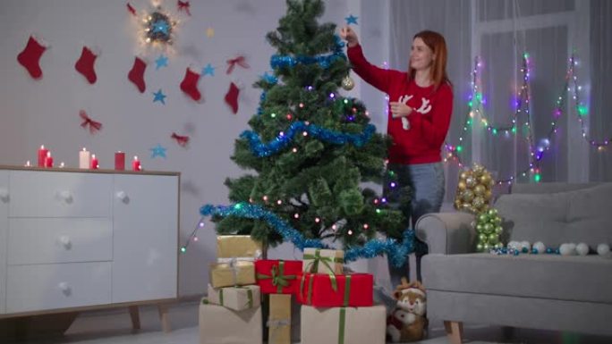 年轻女子正在为新年假期做准备，穿着红色毛衣的女孩通过在人造树枝上挂球来装饰圣诞树，树下有很多礼品盒