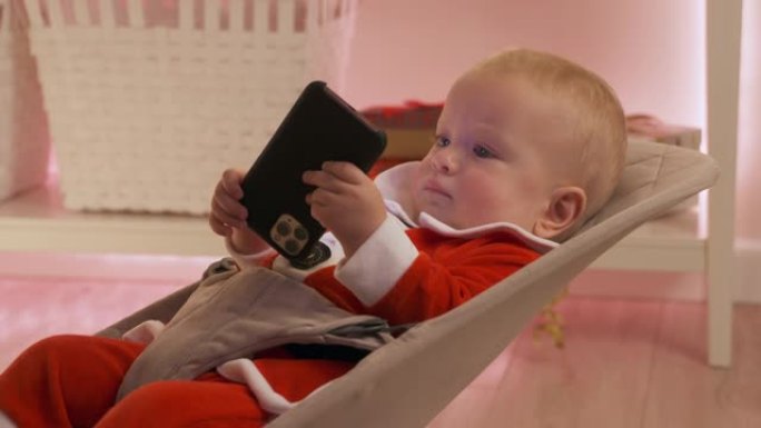 穿着圣诞老人的孩子在除夕夜用智能手机玩得开心，快乐的孩子庆祝他的第一个新年。可爱的男婴拿着手机看着触