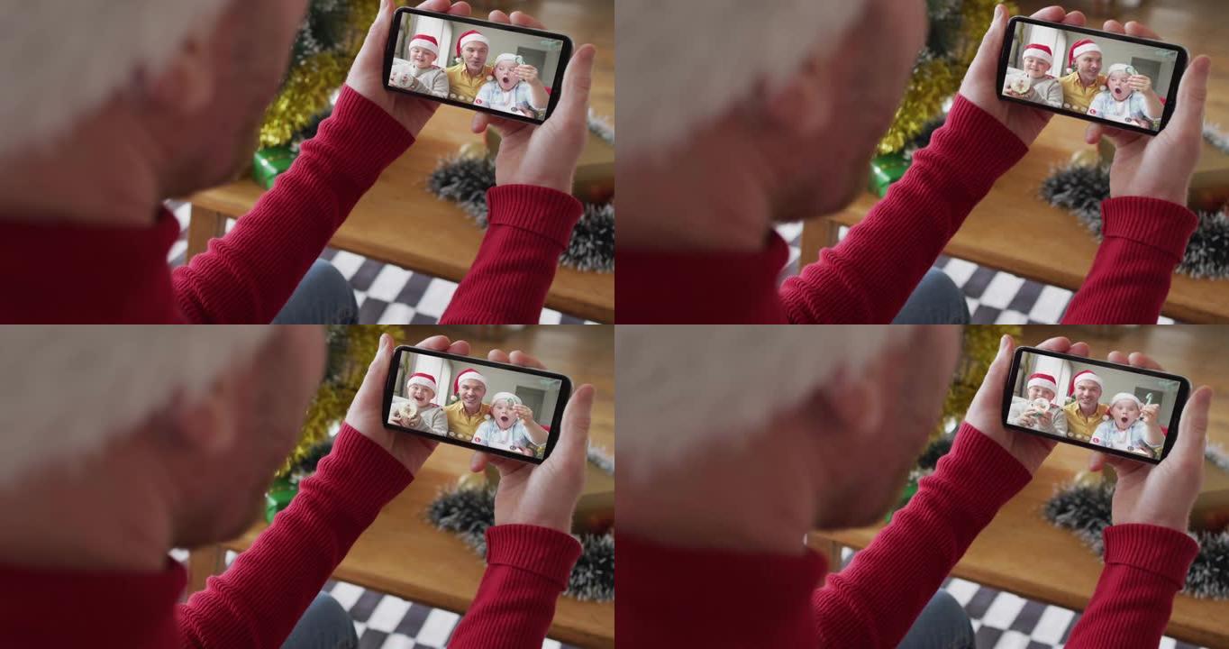 戴着圣诞老人帽子的白人男子使用智能手机进行圣诞节视频通话，屏幕上有微笑的家人
