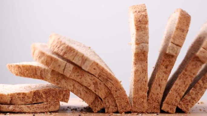 关闭全麦杂粮面包切片落在白色背景的木桌上，慢动作。面包，一片食物，健康的食物概念。