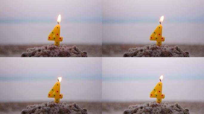 四号蜡烛在棍子上插入沙子和燃烧。模糊海浪背景下的沙子点燃蜡烛。模糊的蓝色棕色背景上的绿色燃烧蜡烛。生