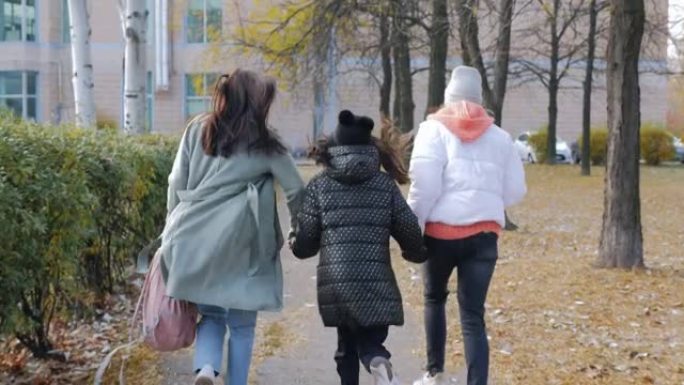 一个有两个女儿的女人急忙上学，从女孩的后面和母亲一起沿着秋天的小巷奔跑。